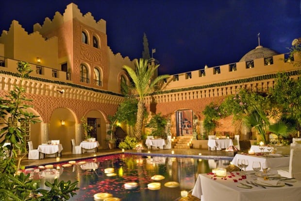 Courtyard with pool and dining tables at night at Kasbah Tamadot, Morocco